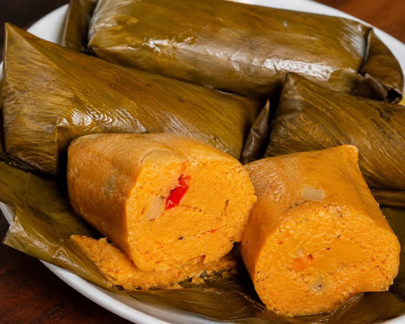 Steamed Nigerian moi moi bean pudding wrapped in banana leaves, sliced open to show the orange interior